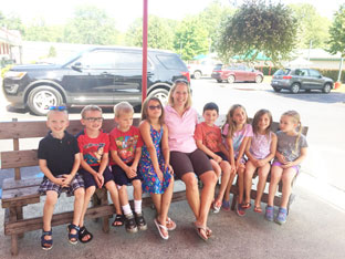 teacher sits on a bench with a group of kindergarten students