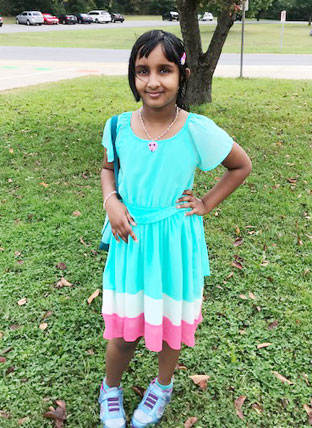 Indian girl in blue dress stands on school lawn