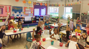 group of students in a classroom hold up their apples