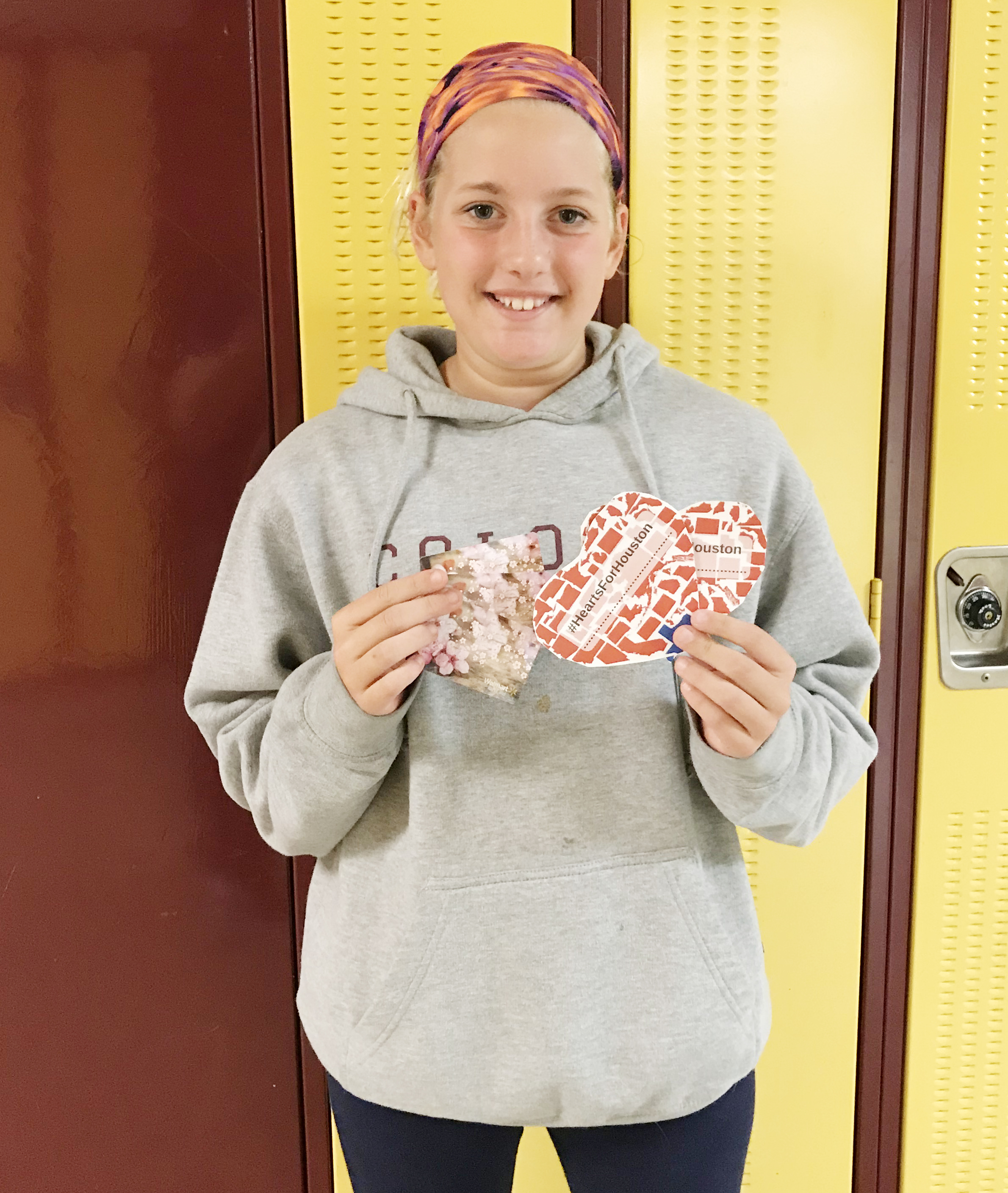 a middle school girl holds up a paper heart in front of her locker