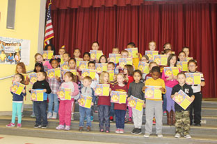 large group of elementary students on stage showing off their award certificates