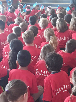 large group of children sitting on the floor showing the backs of their red T shirts