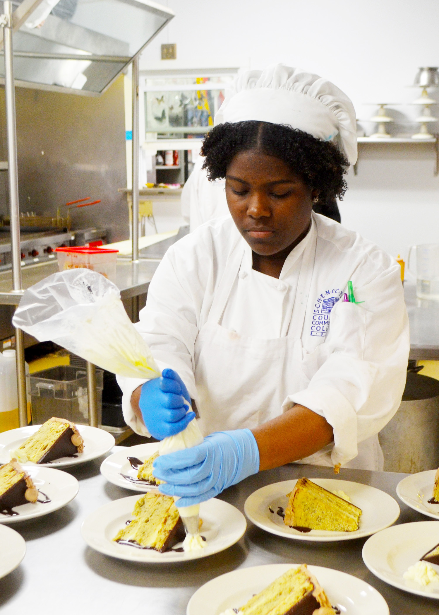 female culinary student puts icing on slices of cake