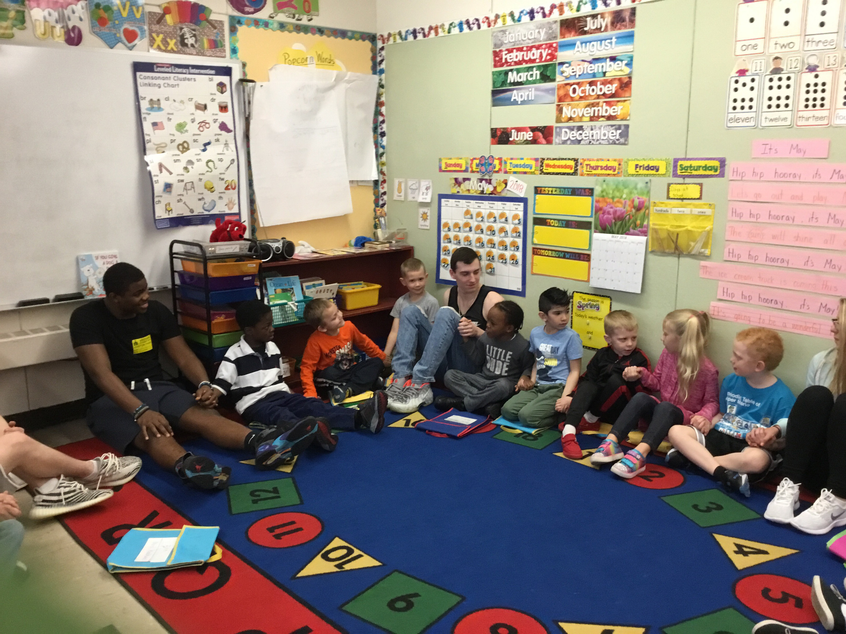 high school students sit on floor helping kindergartners