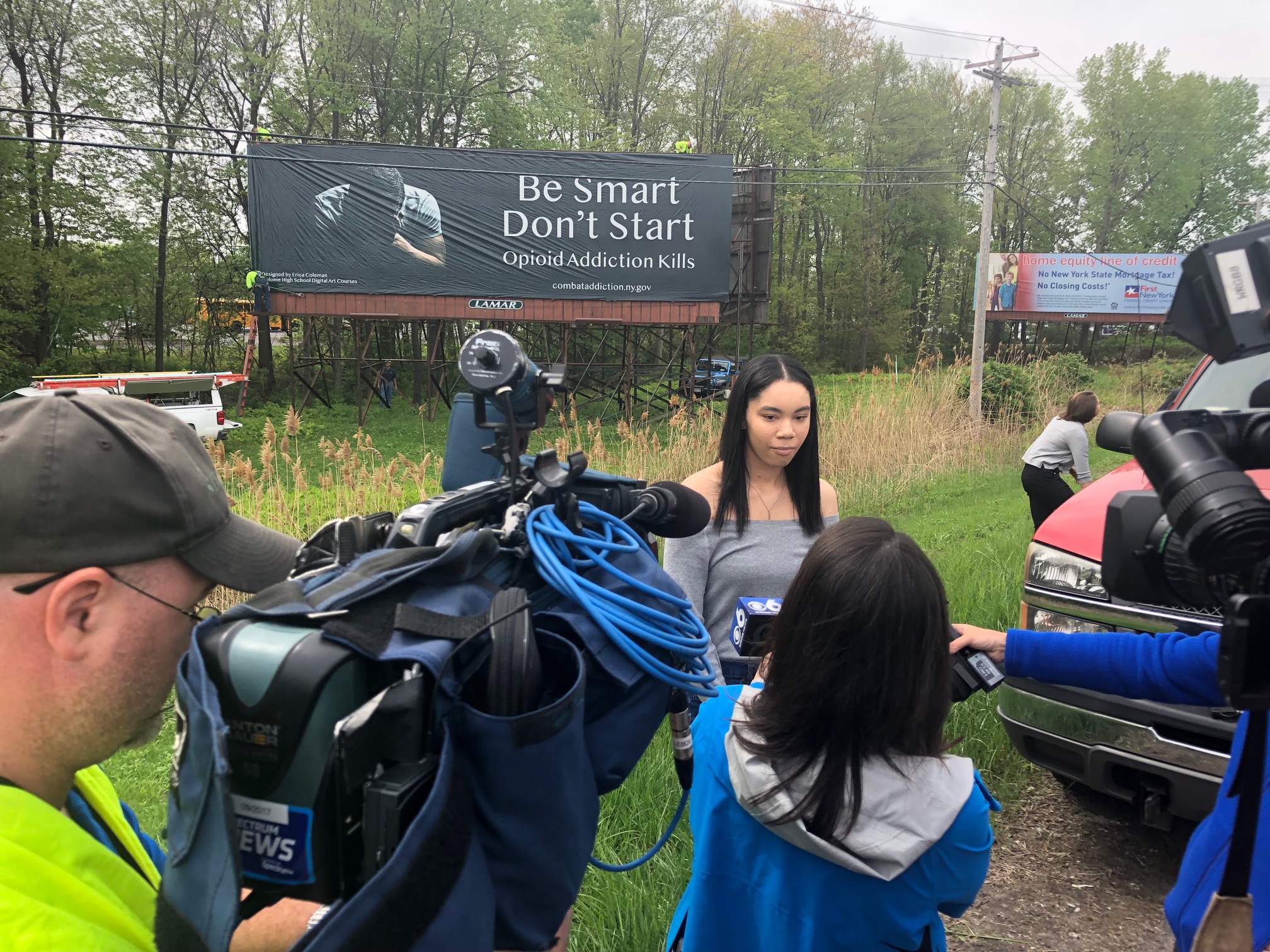 high school student is interviewed by the media standing in front of her winning billboard