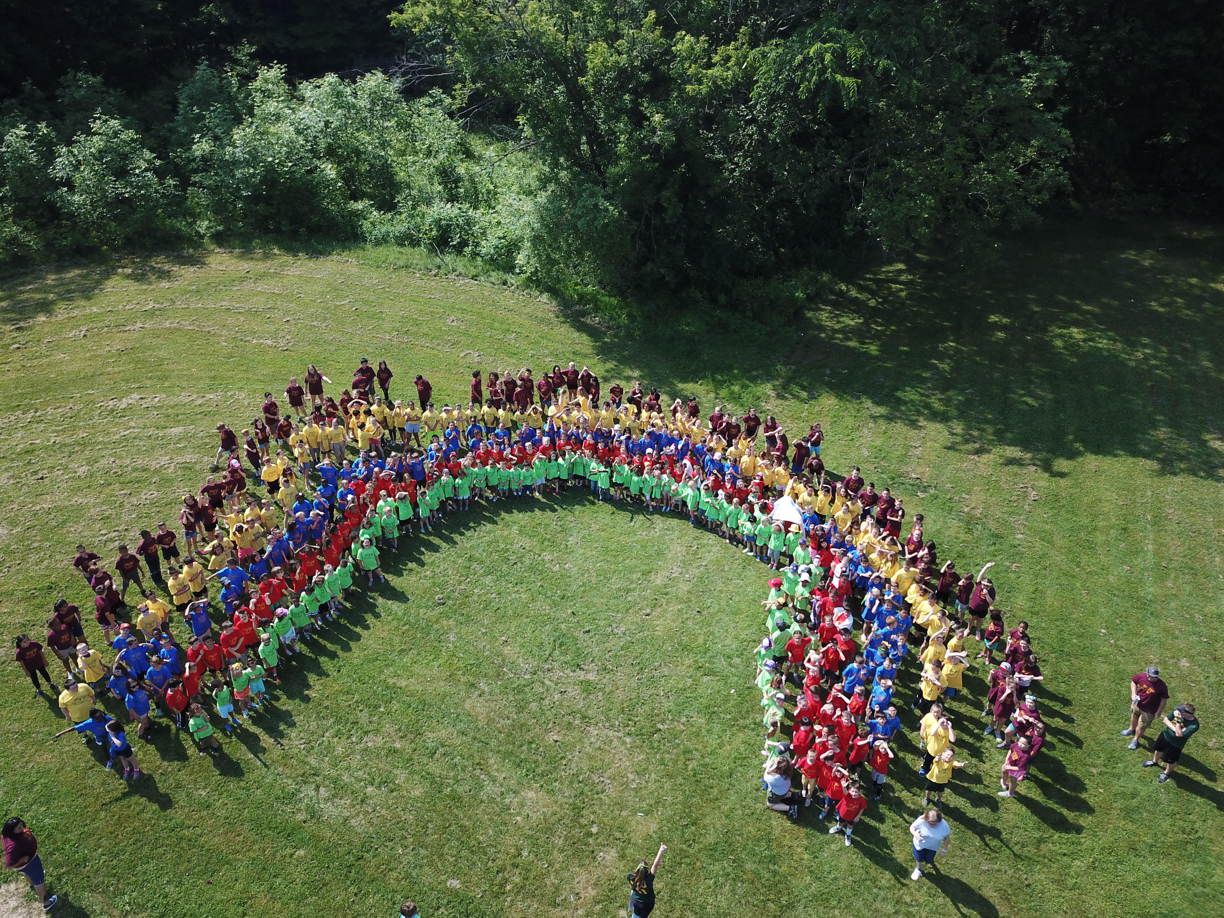 an aerial photo of students forming the colors and shape of a rainbow