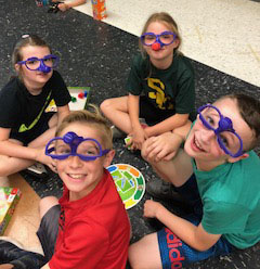 four children on the floor playing a board game wearing funny glasses