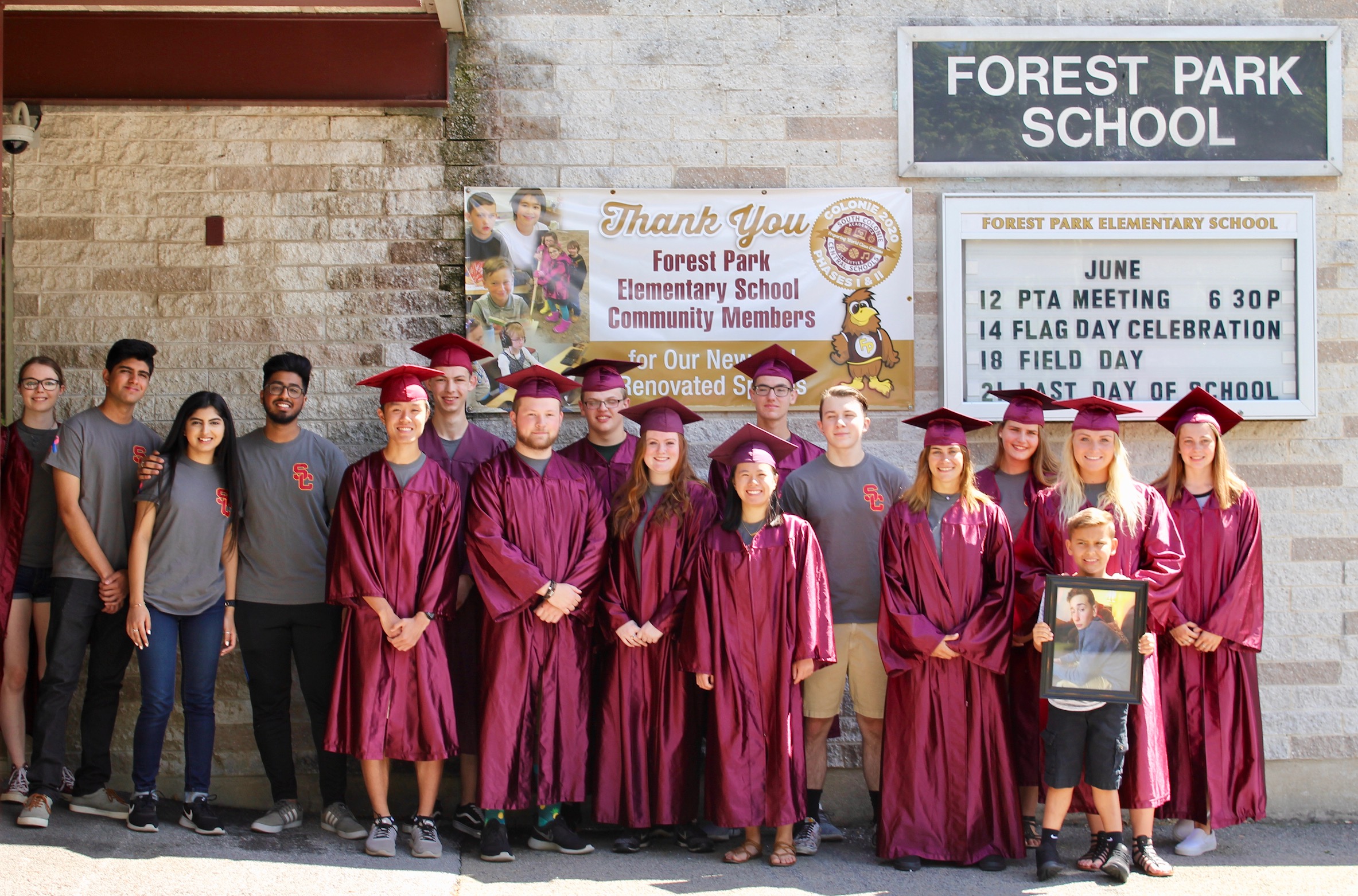 class of 2018 graduates pose as a group in their caps and gowns outside forest park school