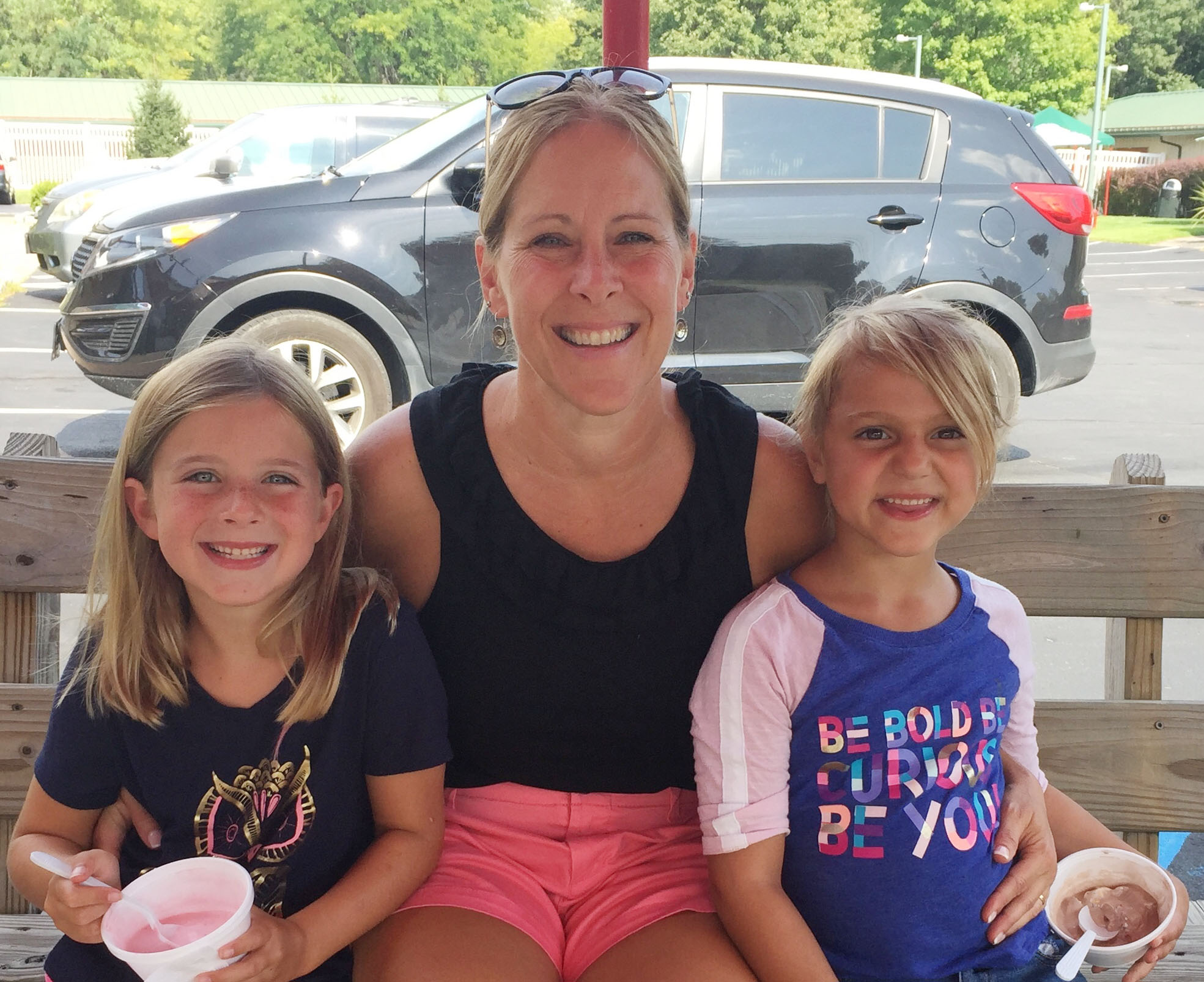 teacher sits with two kindergartners eating ice cream on a bench