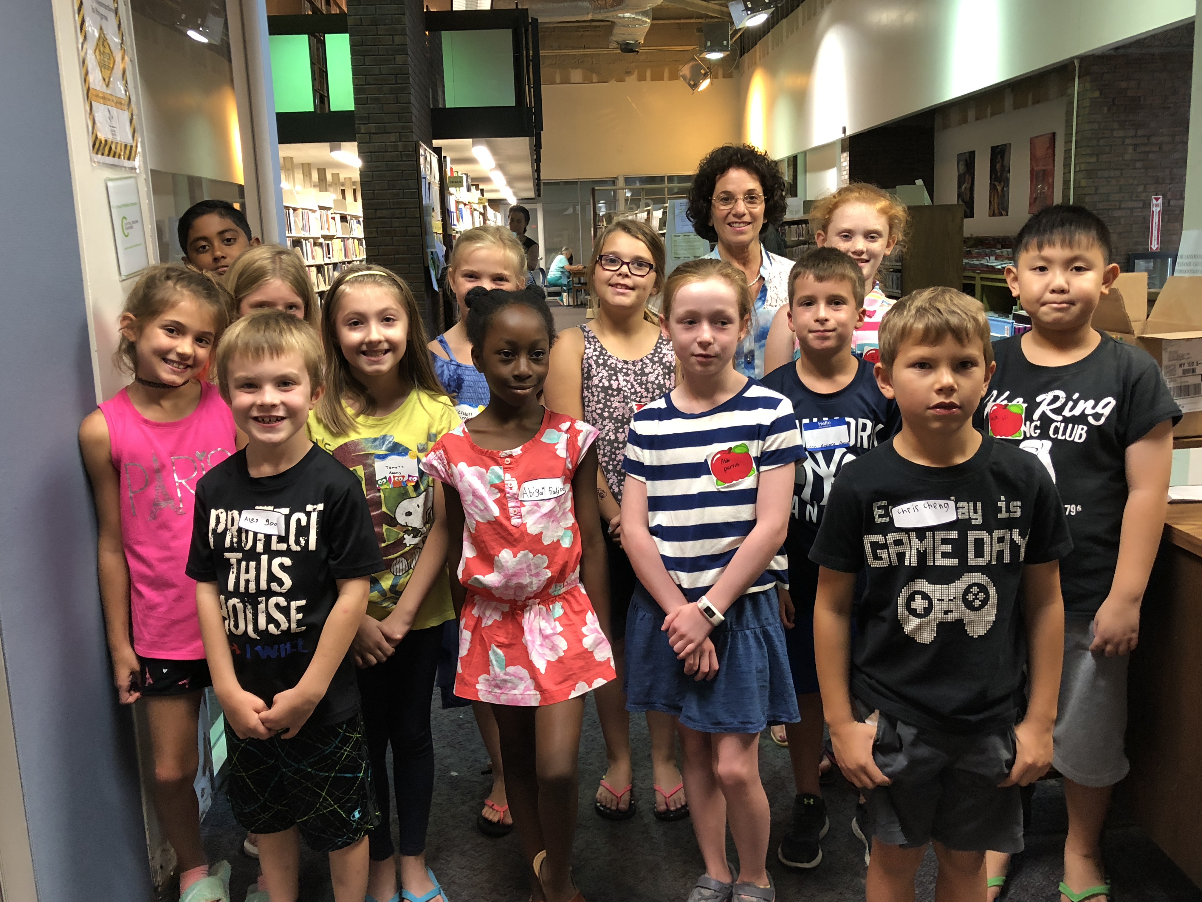 group of 13 third graders gather in the town library surrounded by shelves of books