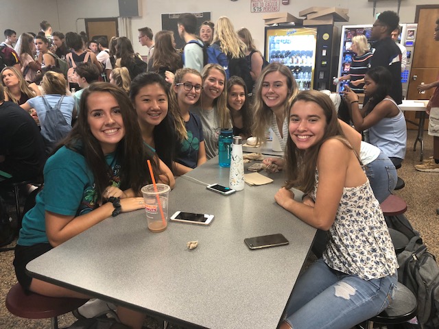 group of high school girls sitting around a cafeteria table smiling for the camera