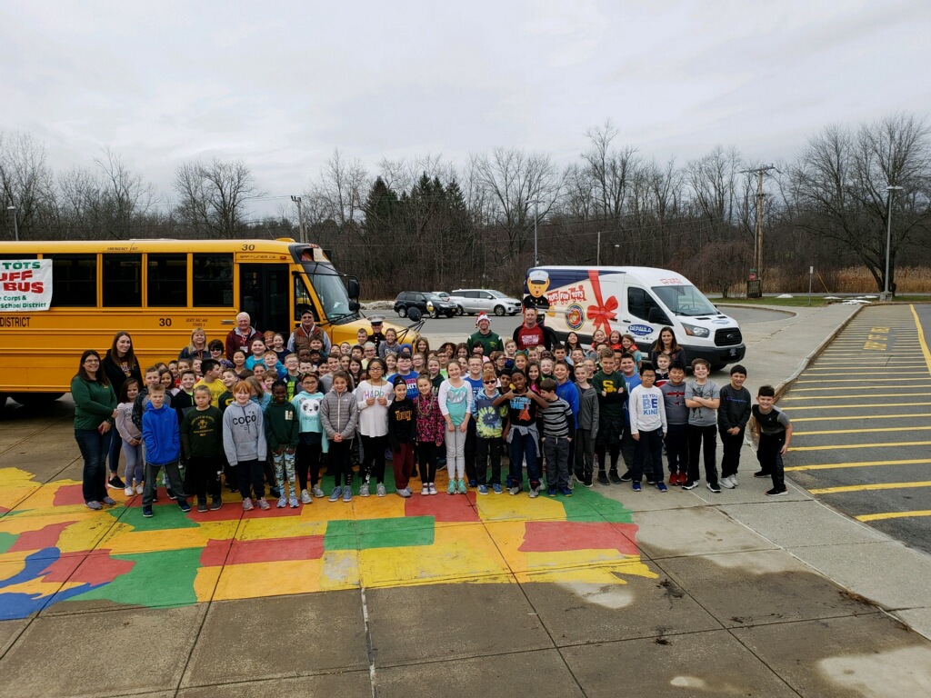 children stand in front of a school bus showing the toys they donated