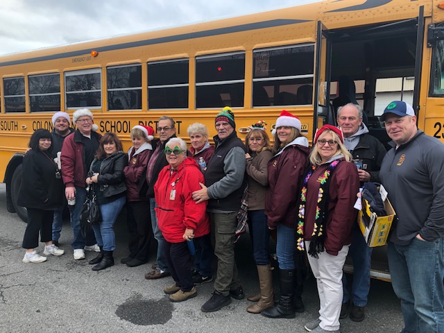 group of bus drivers stand outside yellow school bus