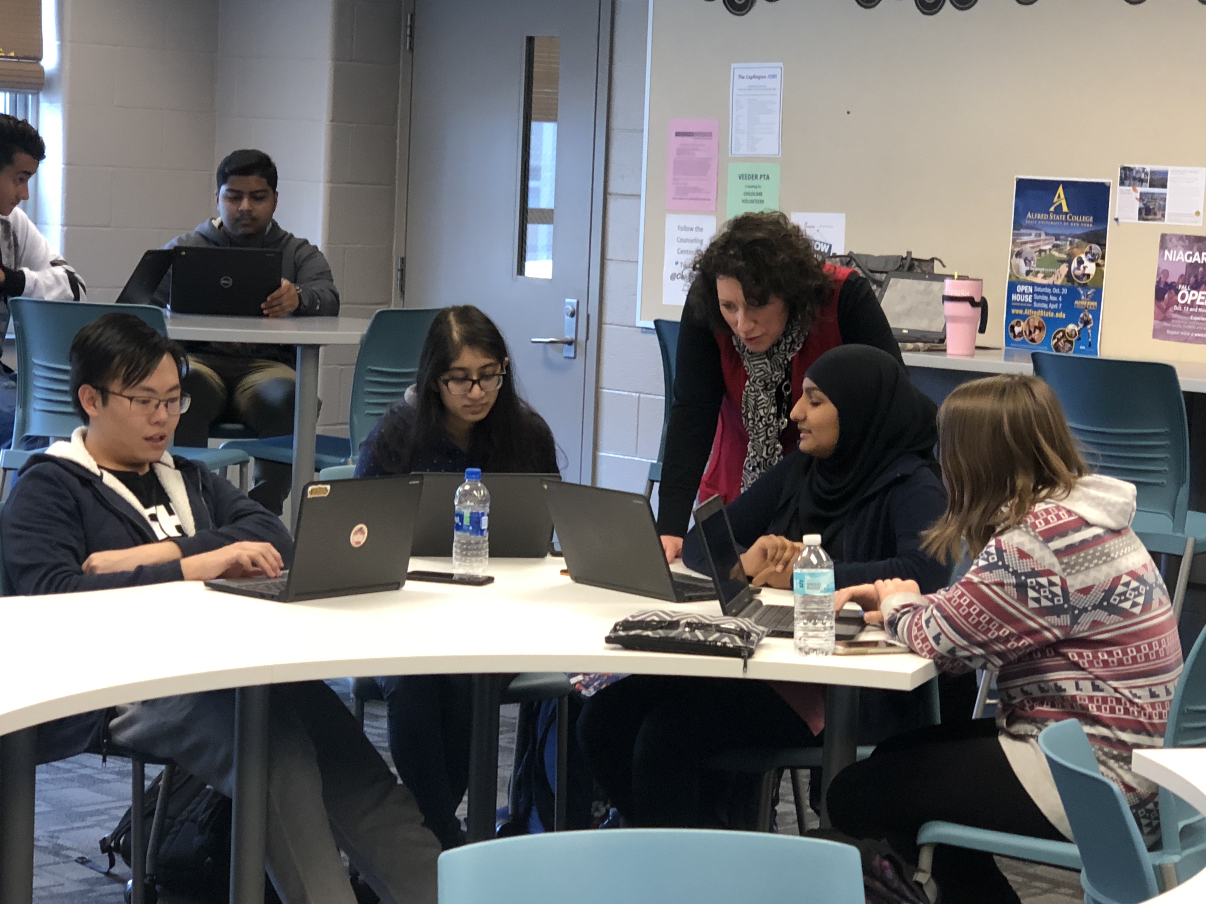 high school students work at a table with a teacher