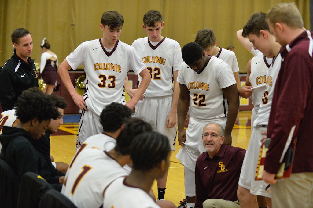 boys basketball players in a huddle with the coach