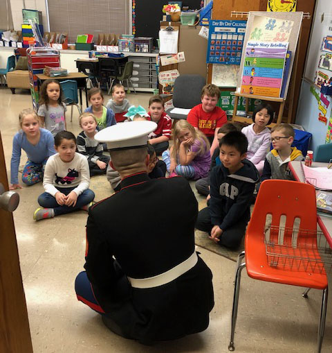 a US Marine in uniform sits on the floor with children