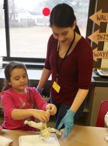 high school students works with an elementary school girl at a table