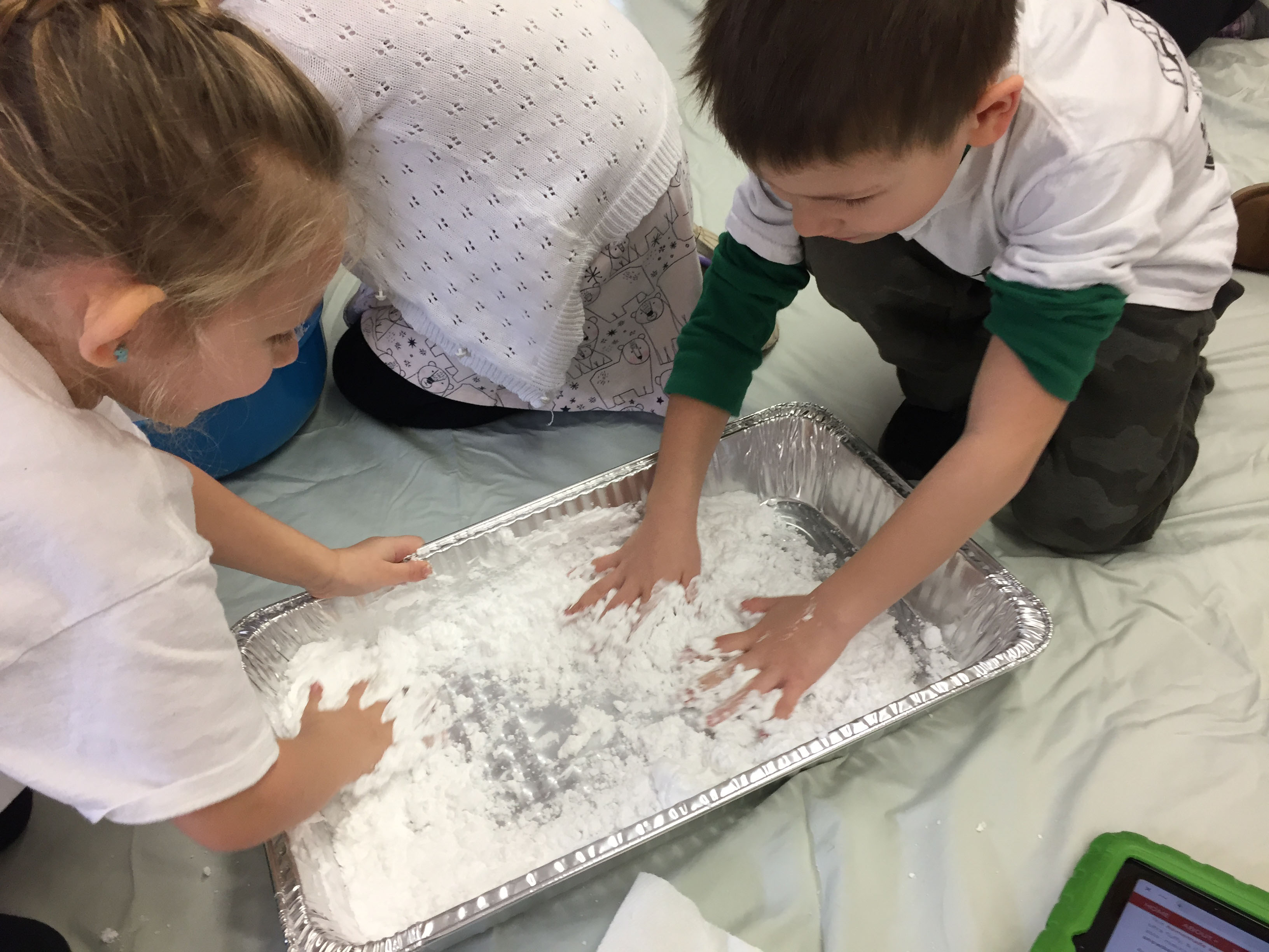 a boy and a girl work together to pack snow in a pan