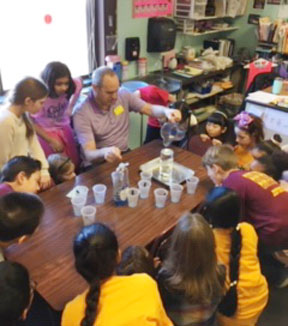 teacher works at desk with large group of students