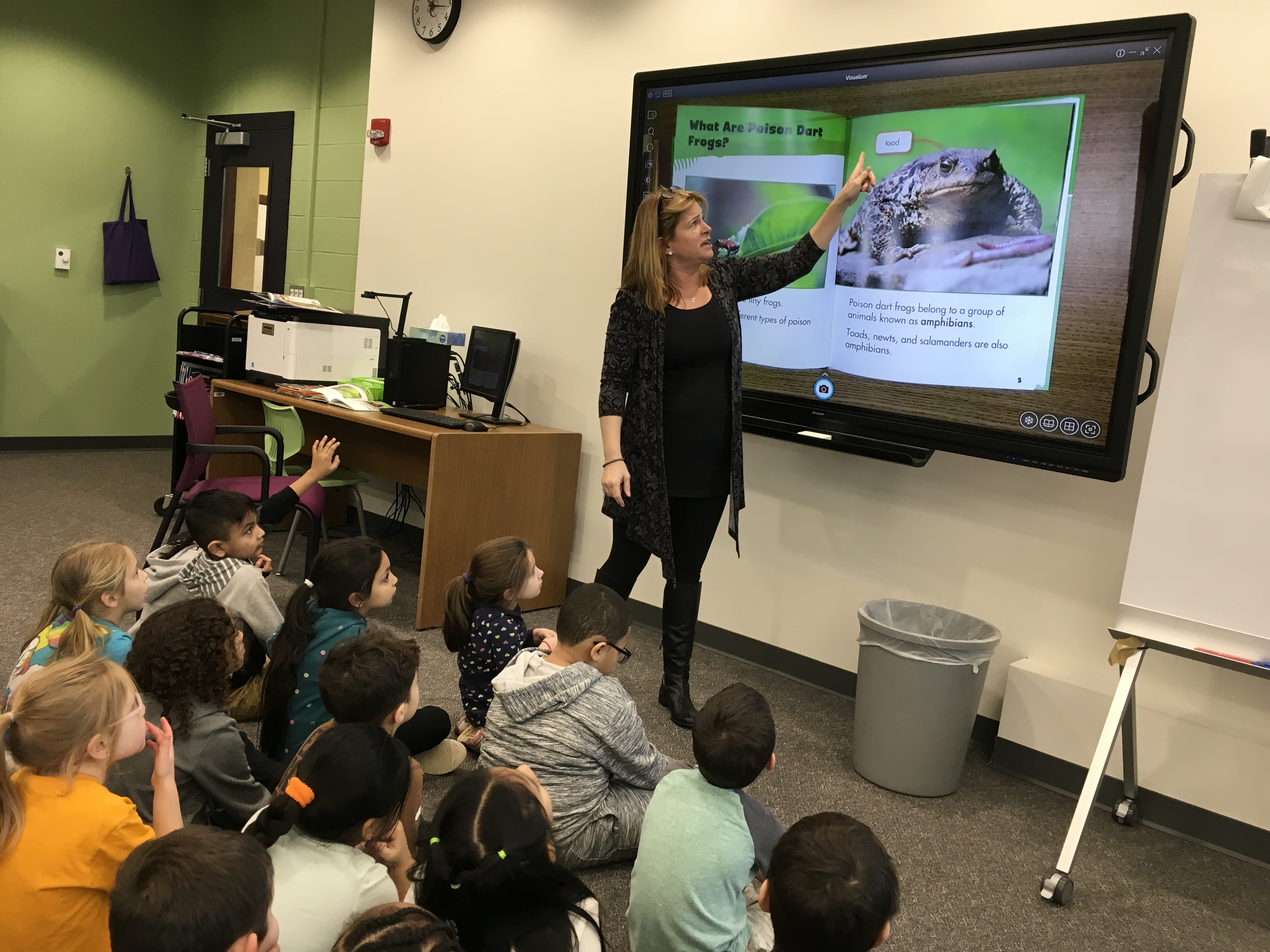 teacher instructed on tv monitor as students sit on the floor watching