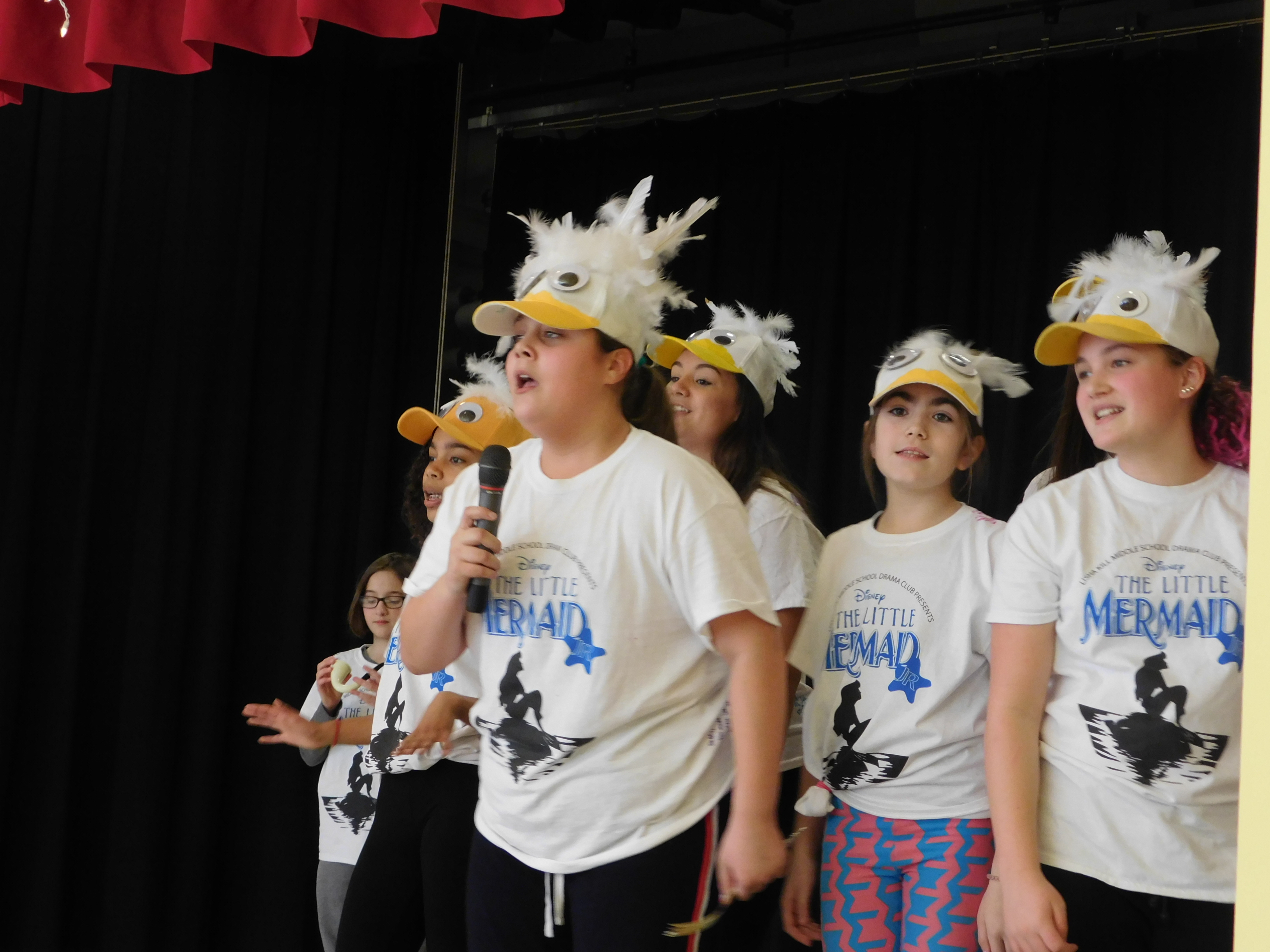 little mermaid cast sings on stage in duck hats