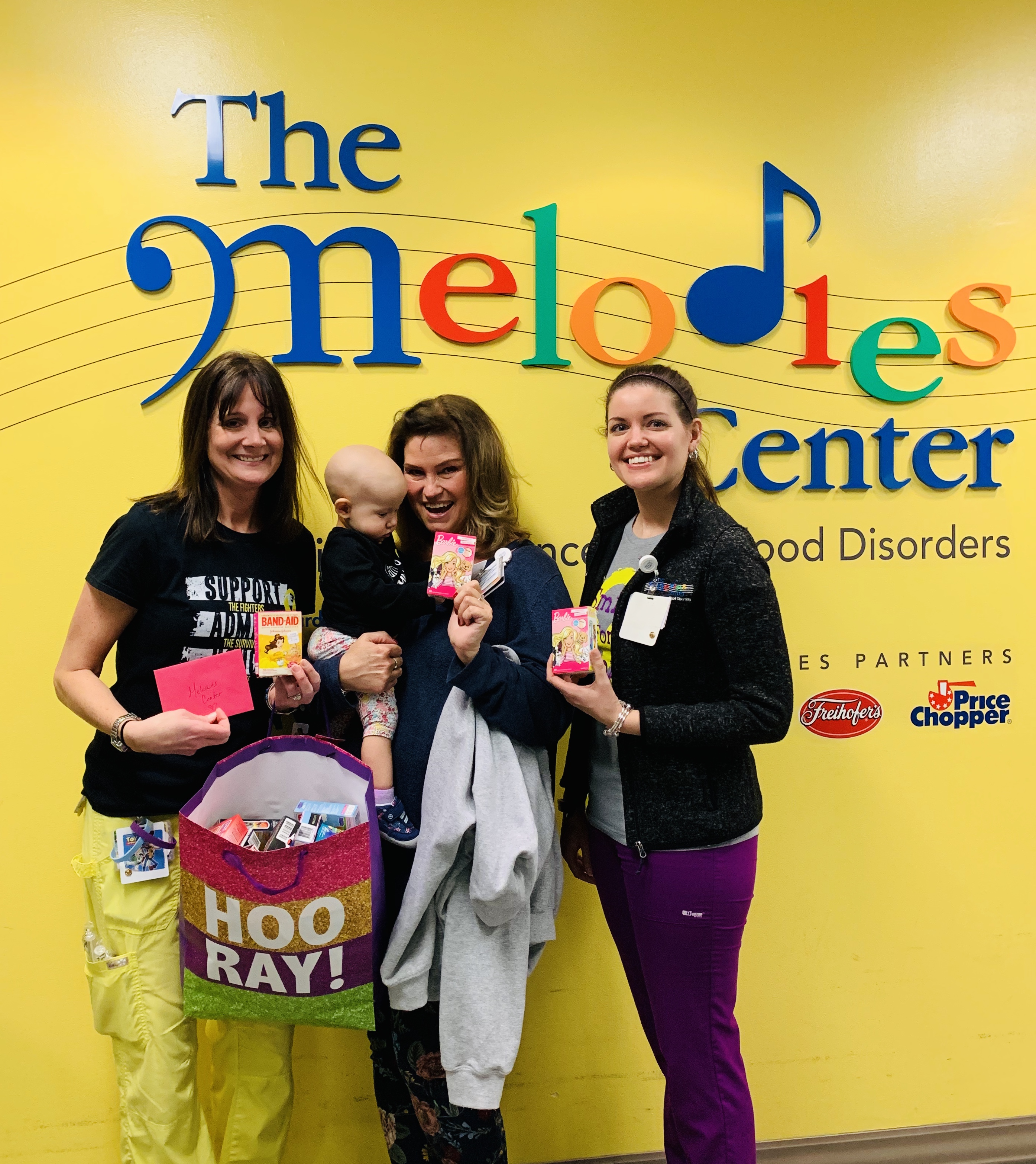 adults and children stand in front of bright yellow Melodies Center sign