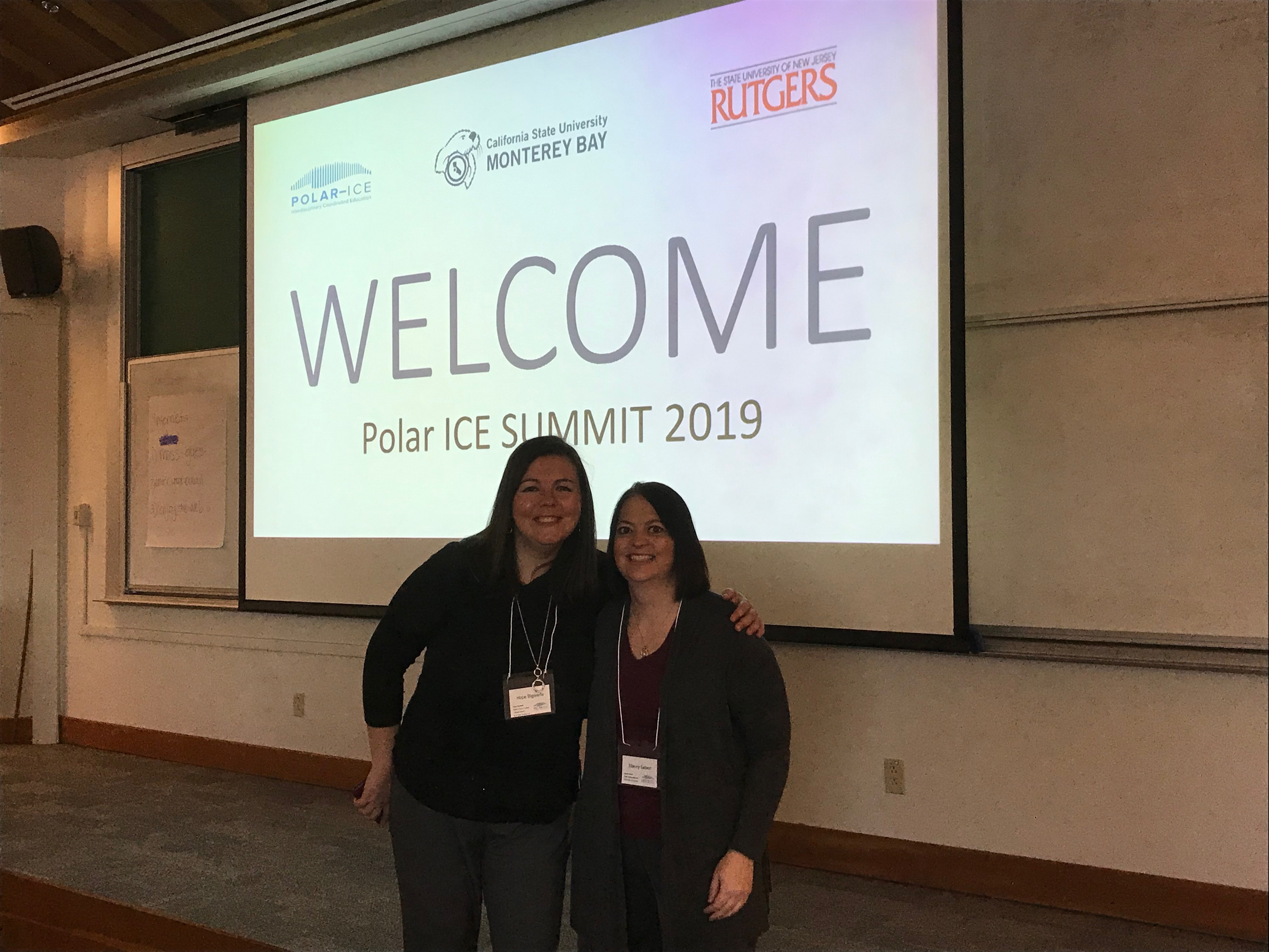 two teachers stand in front of project board