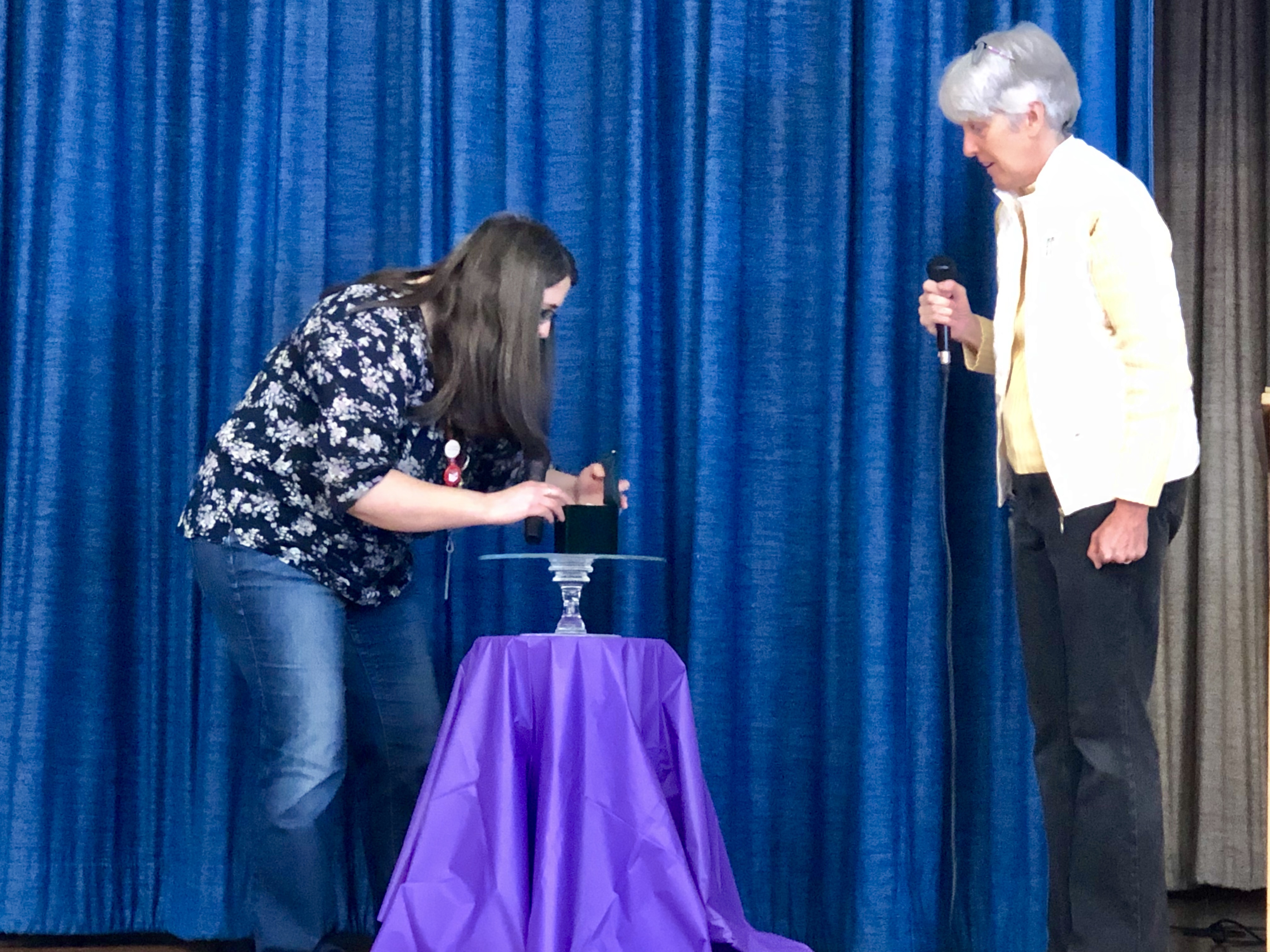 teacher places an emerald on a plate while another teacher watches