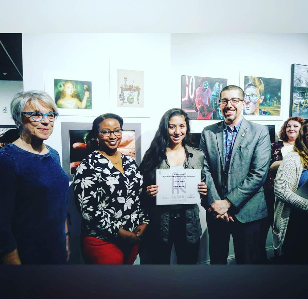 high school student shows her artwork surrounded by the judges