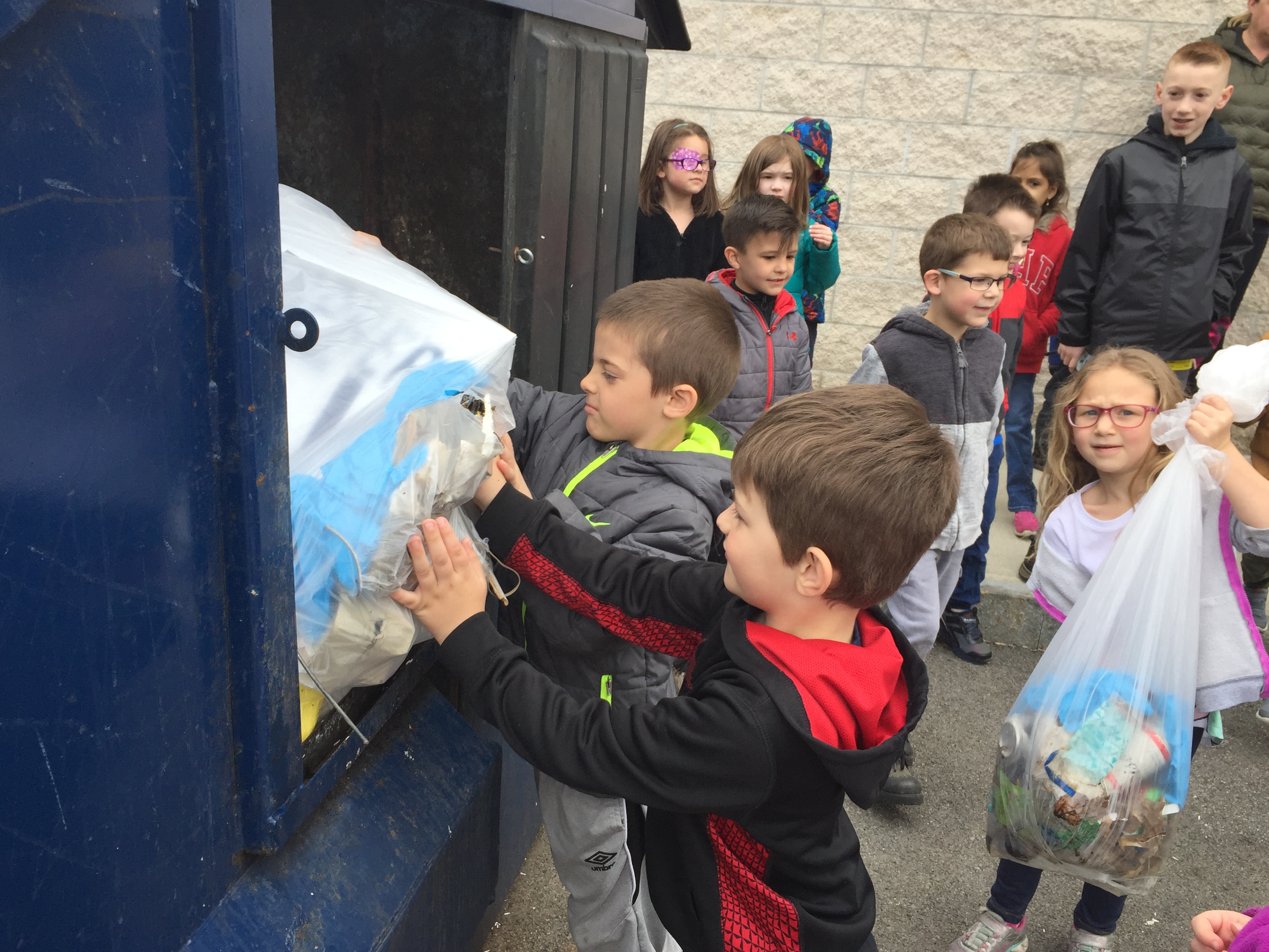 children put trash into a trash dumpster