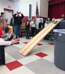 kids roll an egg car down a big long ramp with teacher at end to catch it