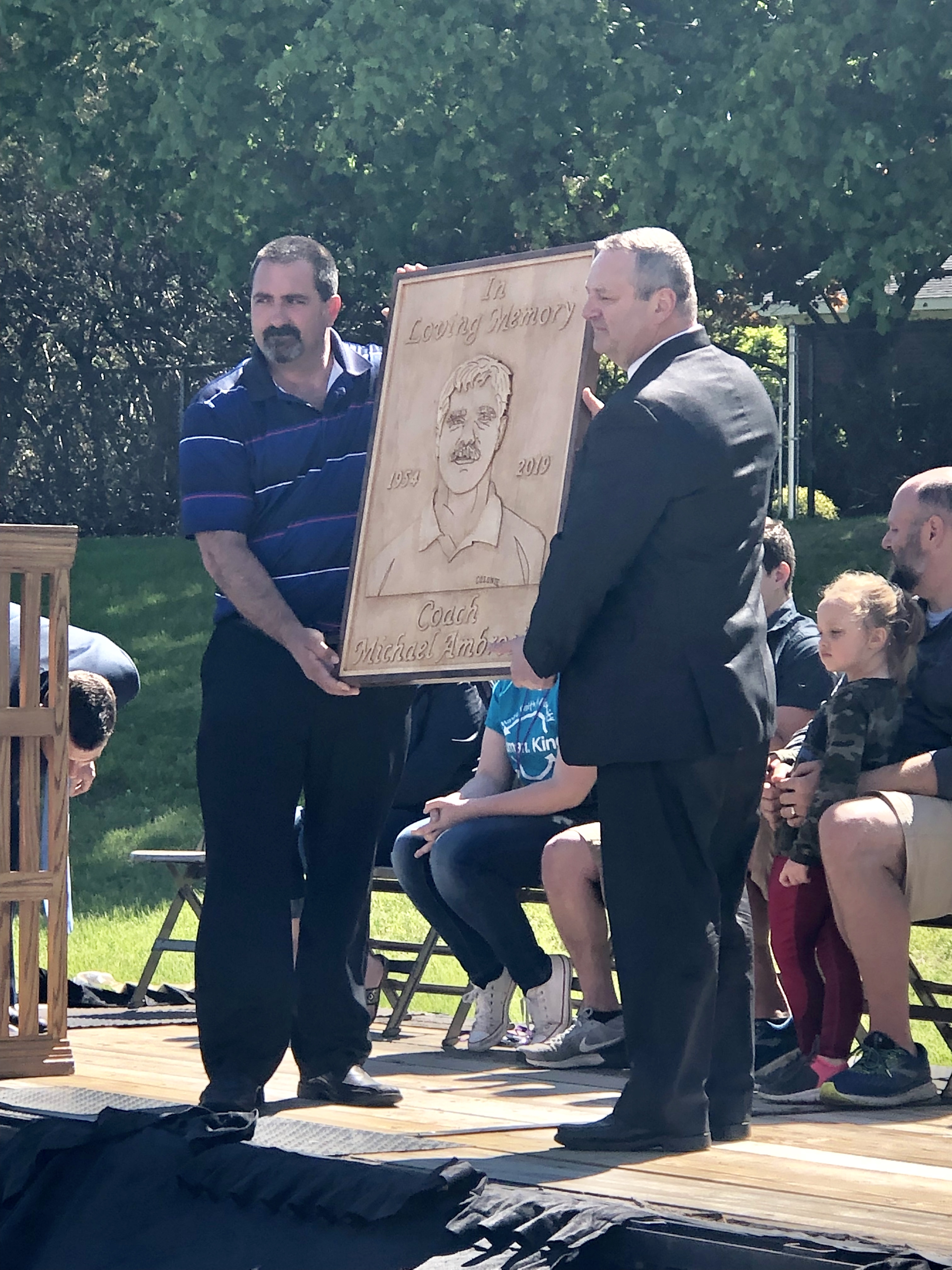 two men hold up a large plaque 