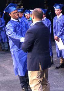 boy in blue gown shakes hands with teacher