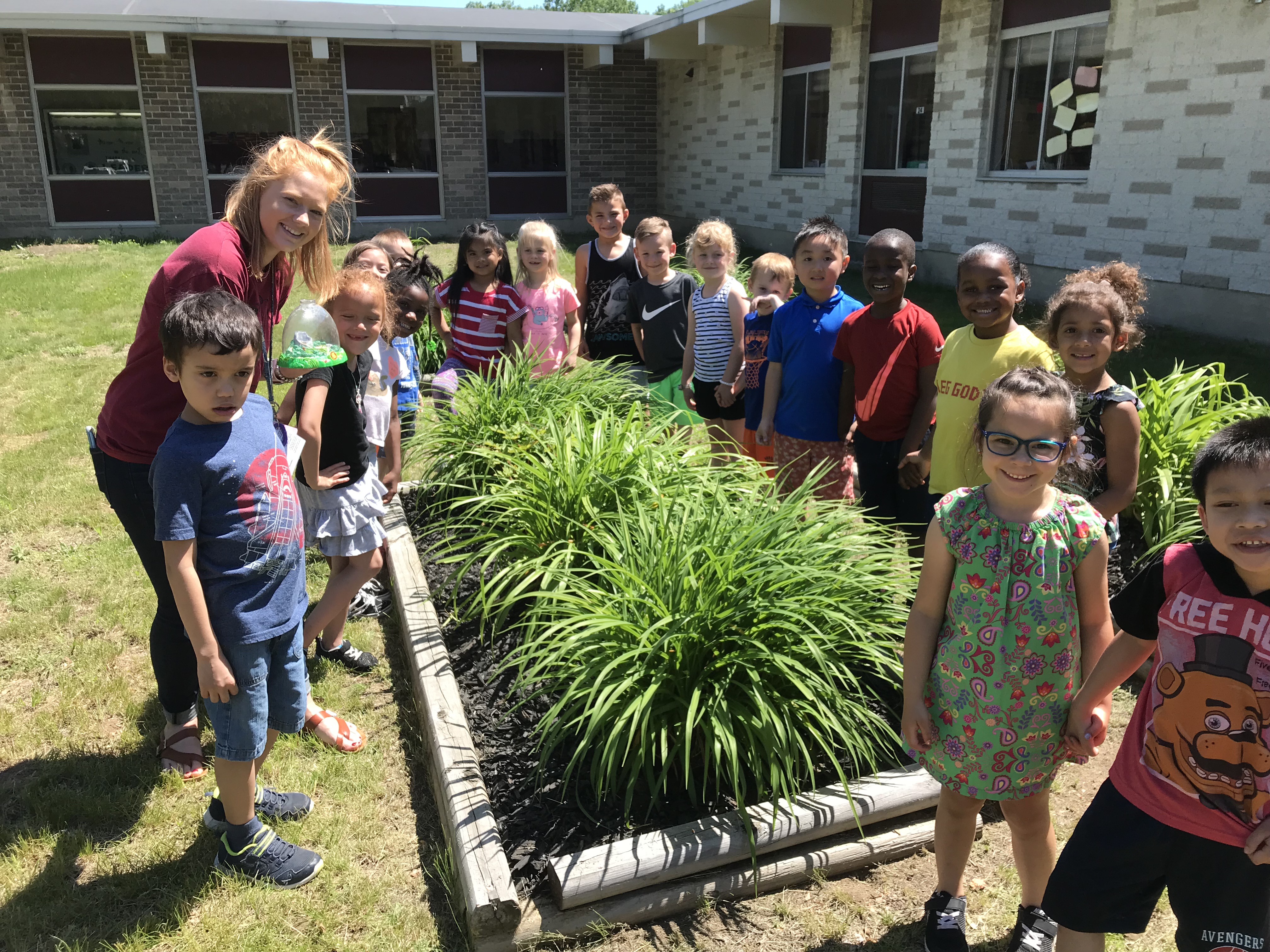 group of kindergartners and their teacher gather around an outside garden