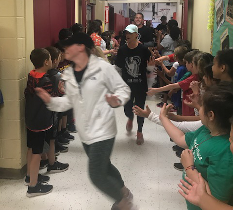 runners go through school hallway while students cheer them on