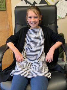 four grader in striped shirt sits in principal's desk chair