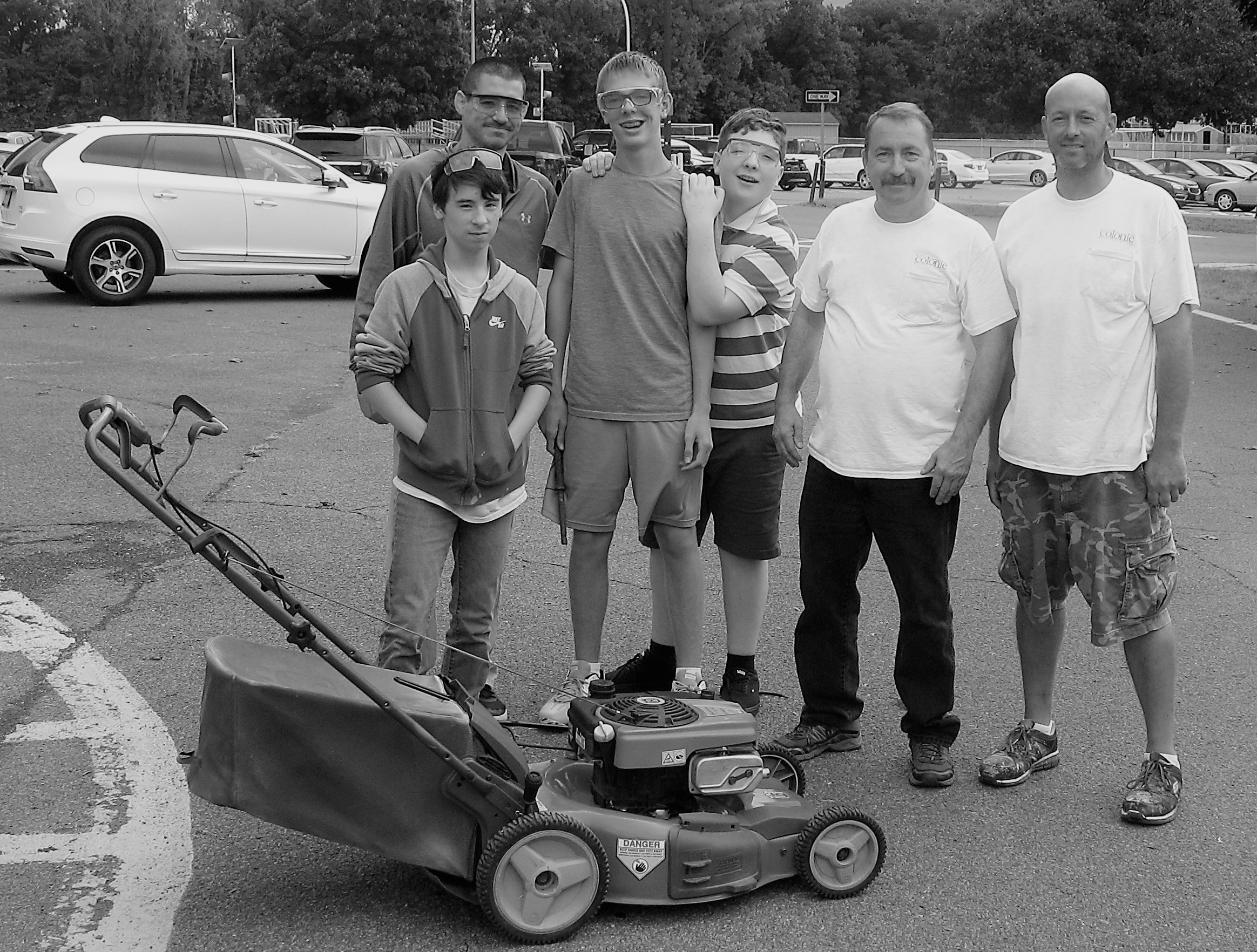 students and staff stand with a lawn mower