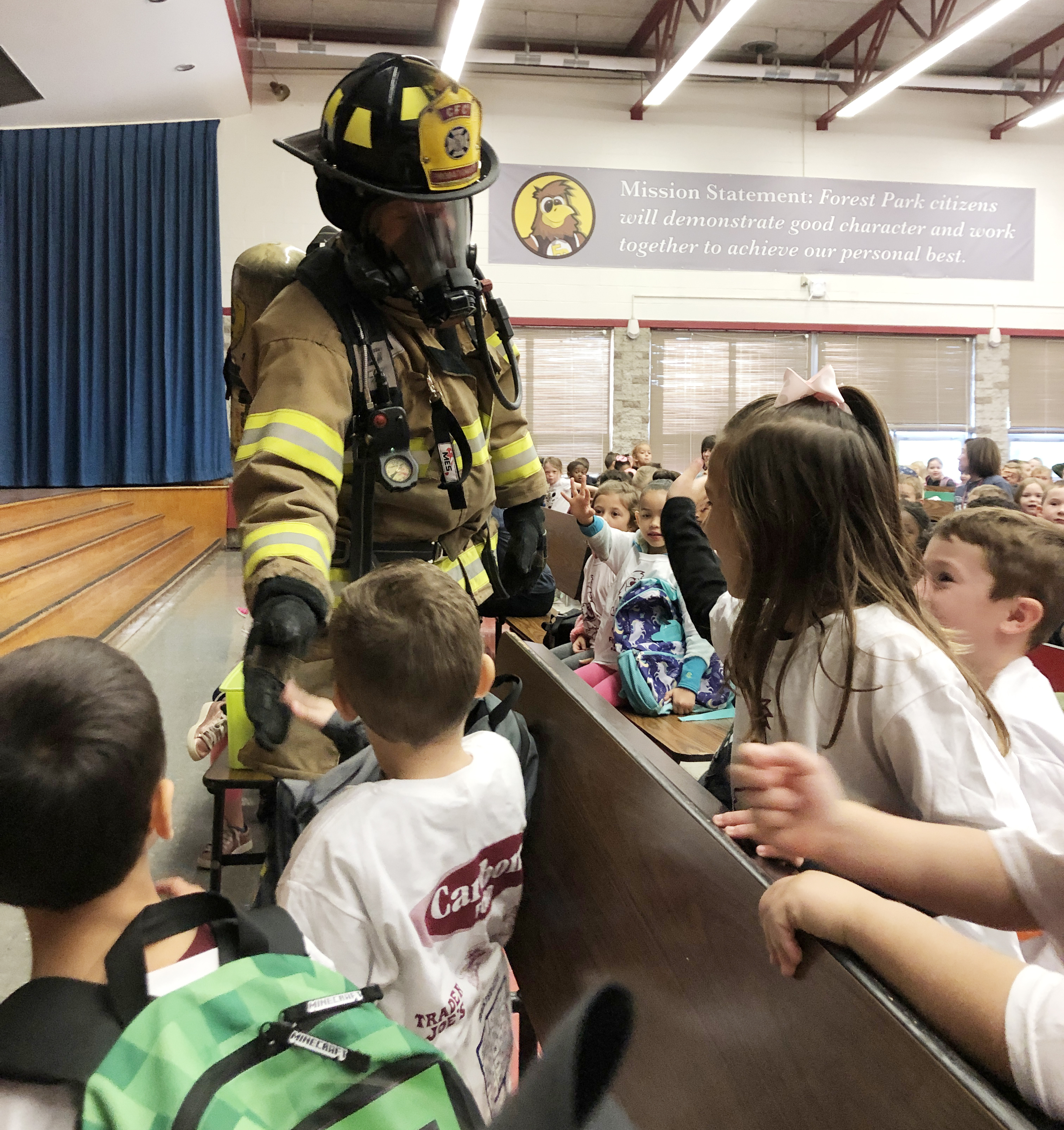 firefighter in full suit and helmet shake hands with students