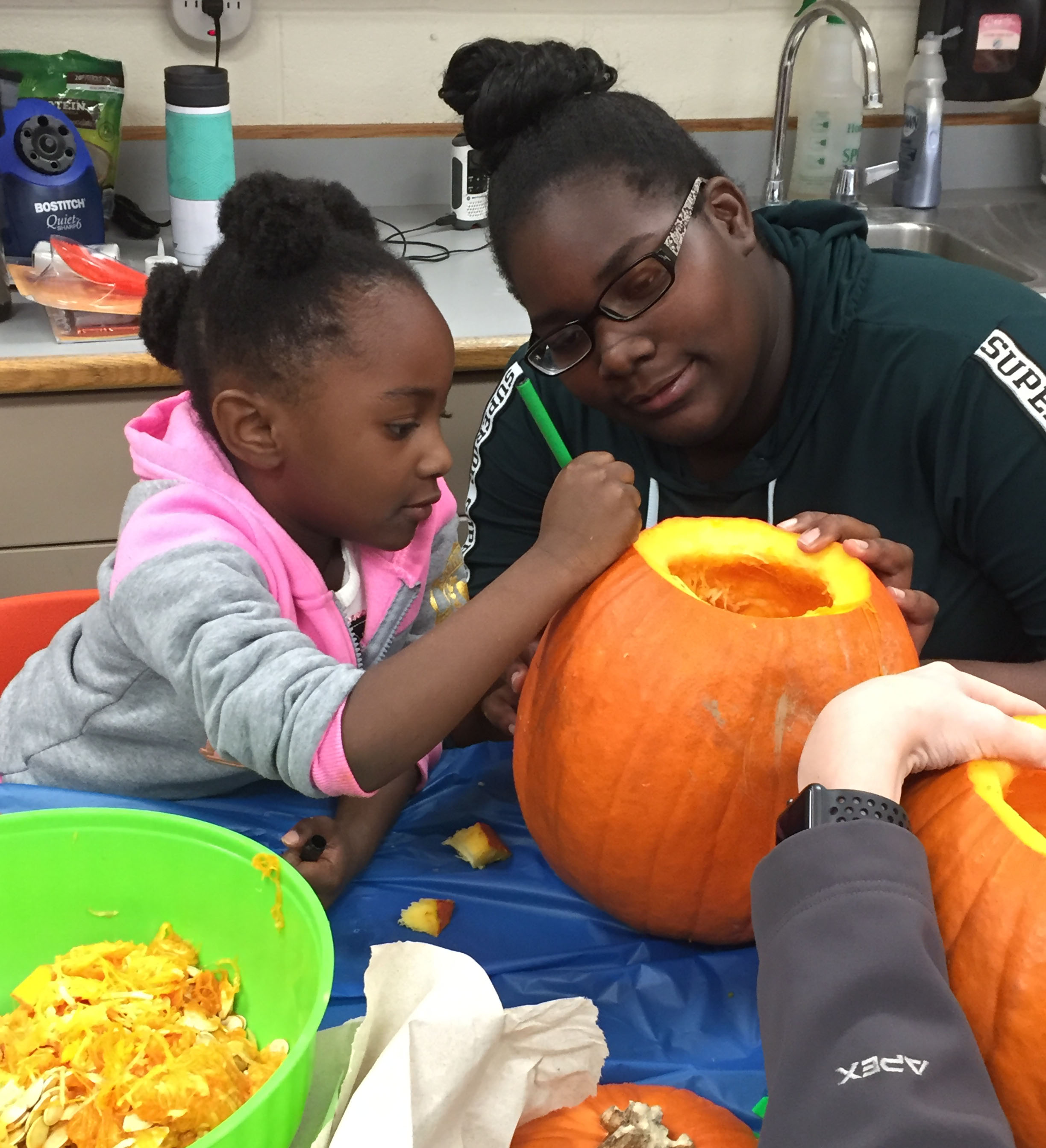 high school student and youngster paint a pumpkin together