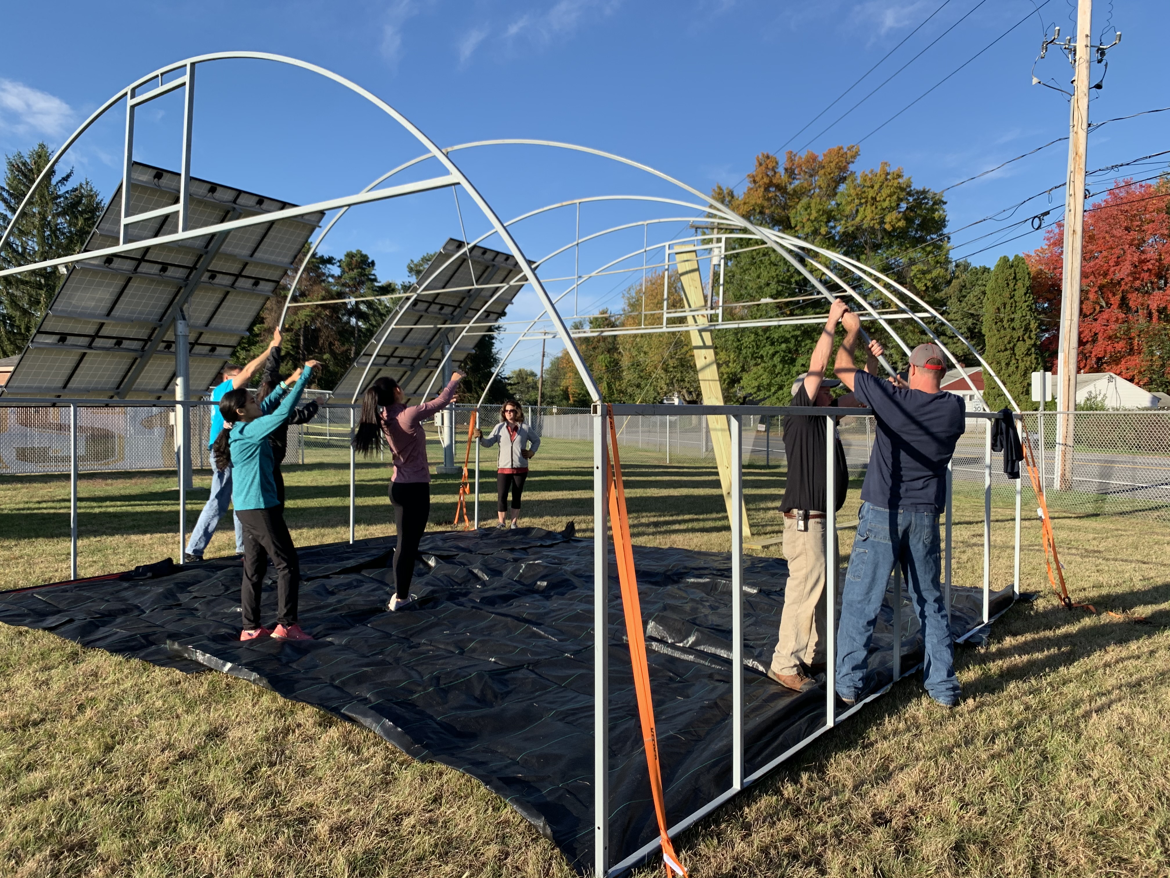 volunteers build the skeleton of an outdoor greenhouse