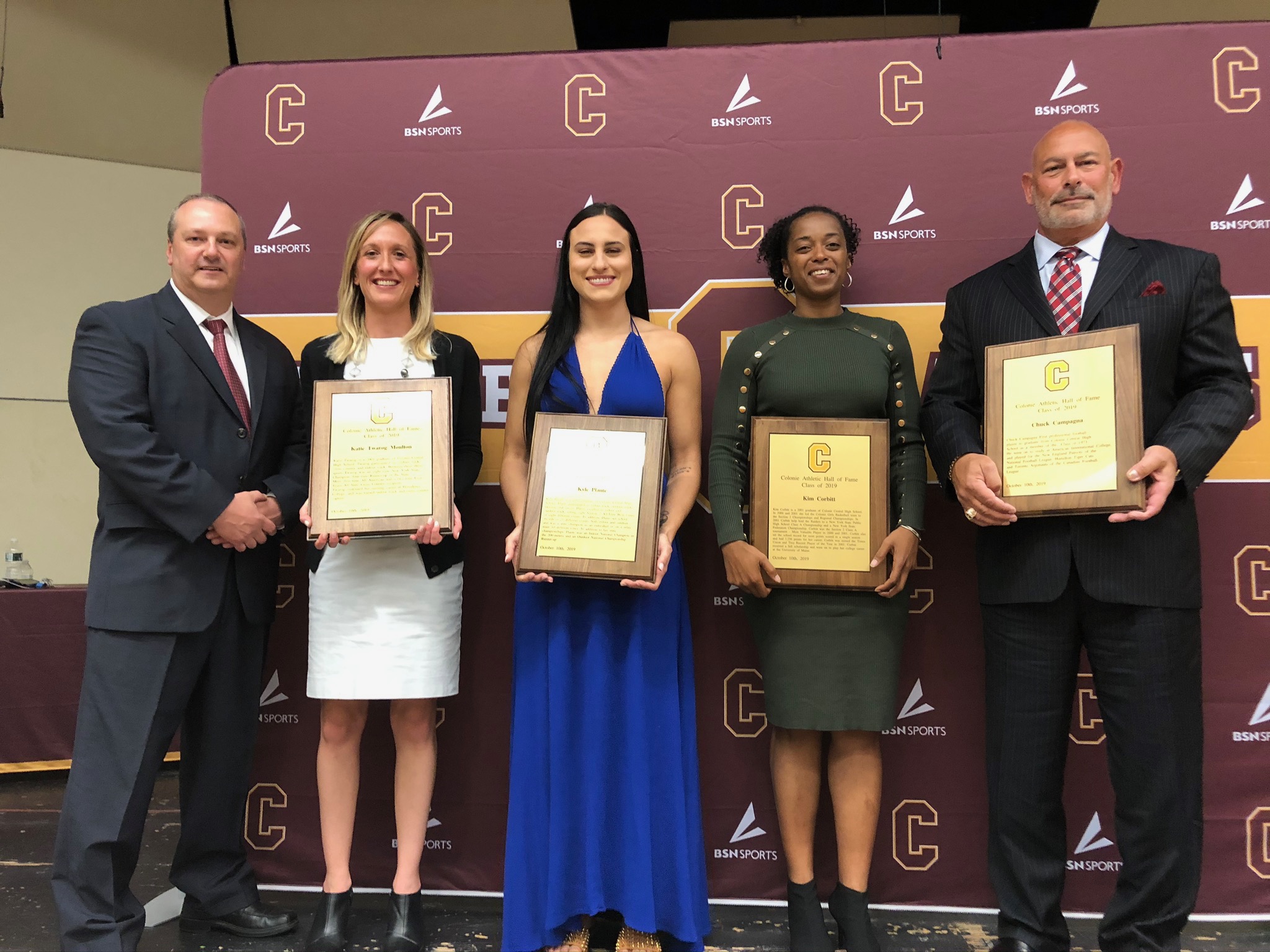 four athletes and the athletic director pose with their hall of fame plaques