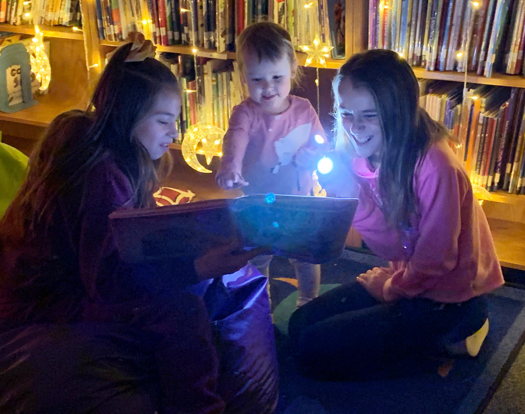 three girls read in the dark by flashlight