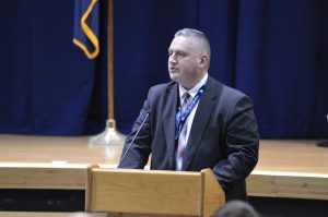 man standing at a podium with a stage behind him.