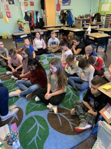 students are sitting on a rug with their eyes closed.