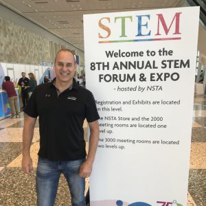 teacher standing at a a conference next to a conference sign