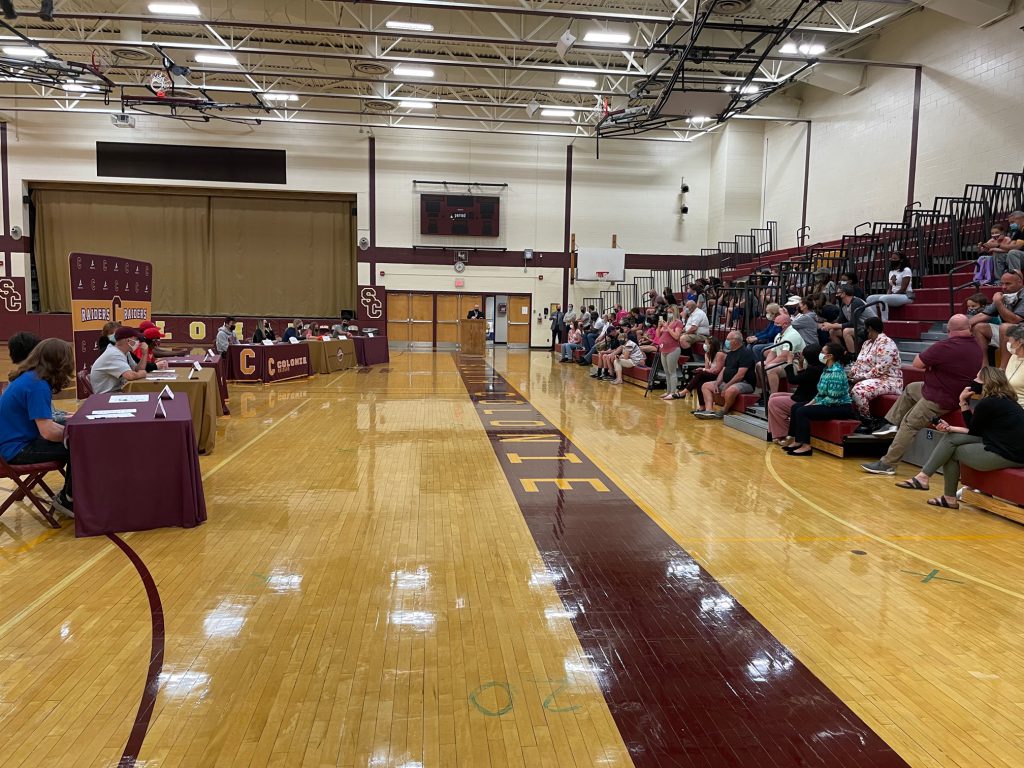 picture of students sitting at tables in a gym with families and friends in the bleachers.