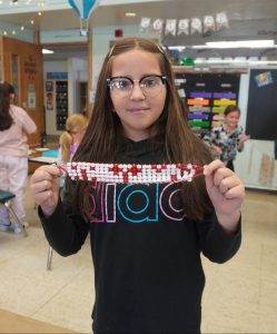 student holds up her beaded belt proudly,