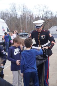 U.S. Marine helps two students put toys in a black plastic bag.