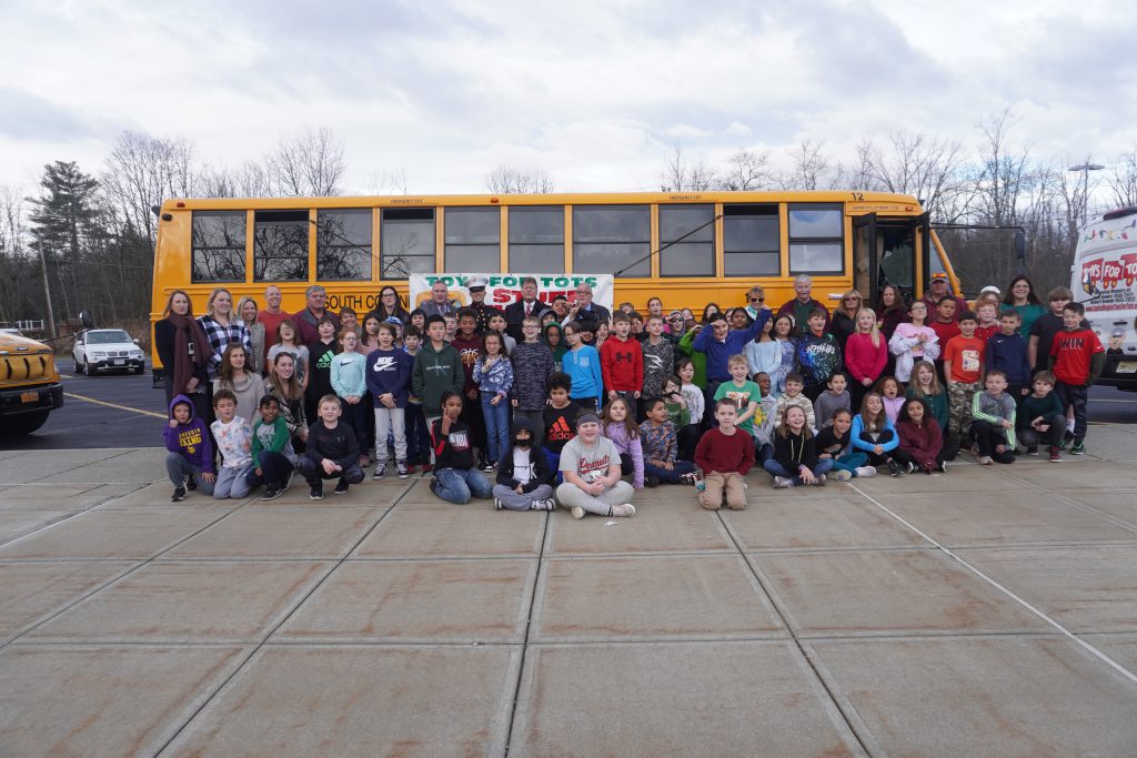 group of students and staff memebrs stand in front of a bus for a photo