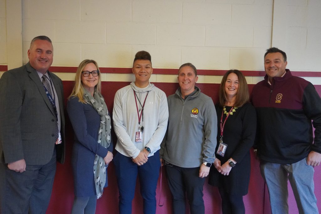 superintendent joined with the principal of the school and a board member pose with three staff members for a photo. 